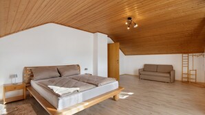 Een slaapkamer met een houten plafond, een bed, een nachtkastje, een bank en een ladder.