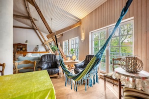 A room with a hammock, wooden furniture, a table with a floral tablecloth, and large windows.