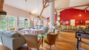 A spacious indoor area with wooden floors, a pool table, and seating arrangements including sofas and chairs.