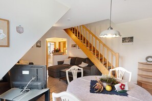 A living room with a television, a dining table with a vase, and a staircase.