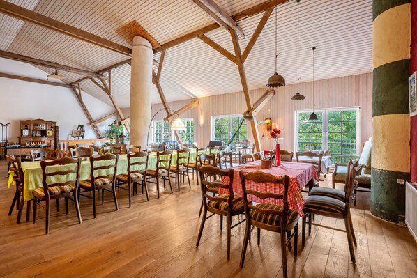Un comedor amplio con mesas y sillas de madera, ventanas grandes y un techo alto con vigas a la vista.