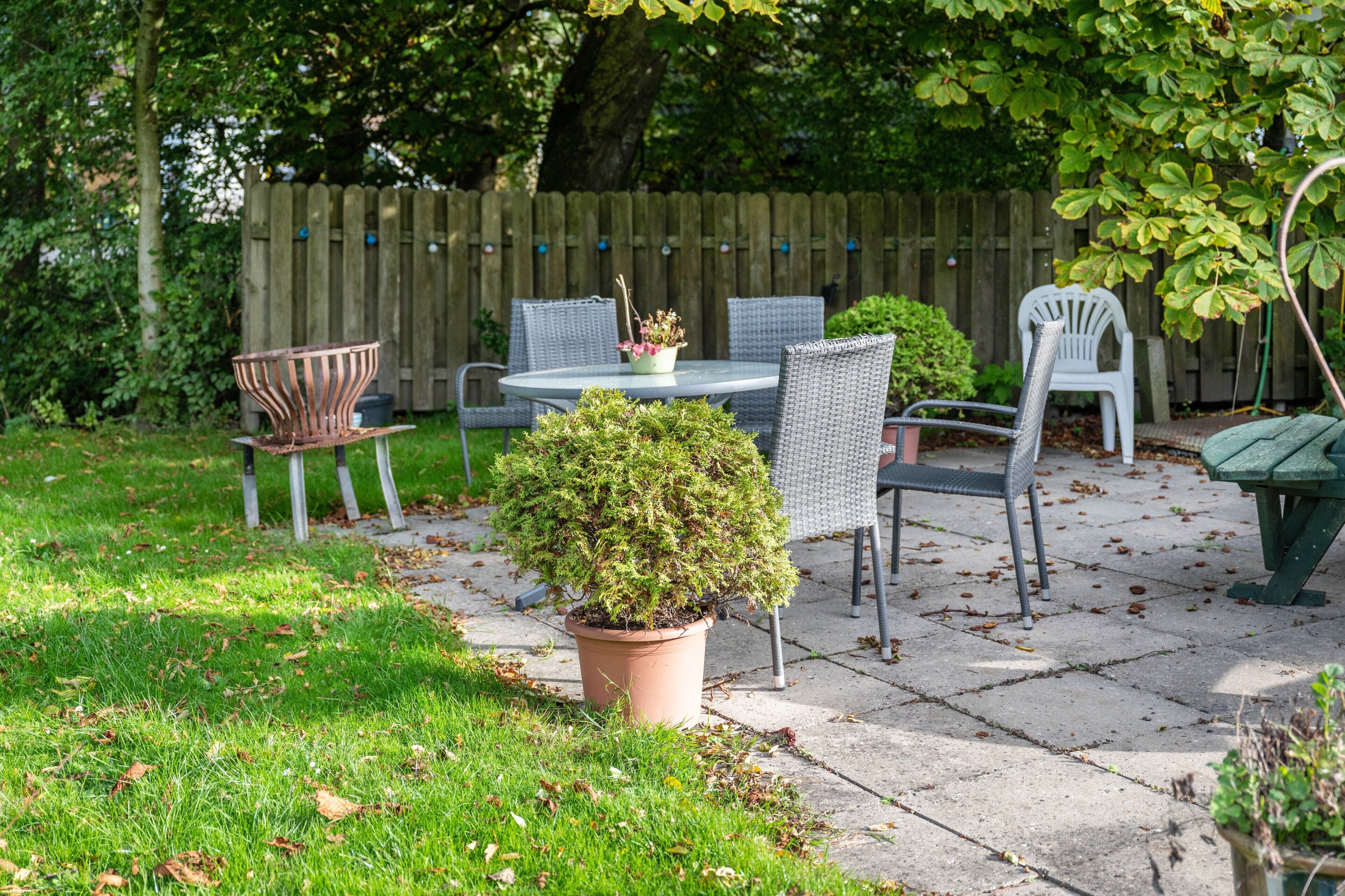 Eine Terrasse mit einem runden Tisch, vier Stühlen, einem Blumentopf und einem Holzzaun im Hintergrund.
