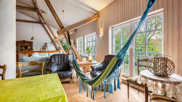 A room with a hammock, wooden furniture, a table with a floral tablecloth, and large windows.