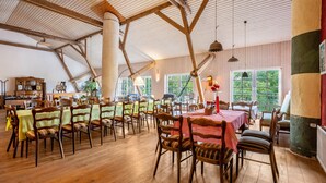 A spacious dining area with wooden tables and chairs, large windows, and a high ceiling with exposed beams.