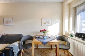 Un salon avec une table en bois, deux chaises, un canapé, un radiateur et une fenêtre avec une lampe.