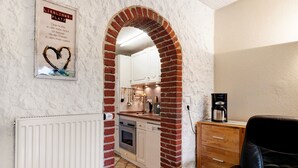 Een keuken met witte kasten, een bakstenen boog en een koffieapparaat.