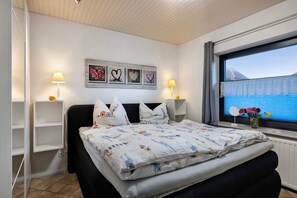 Une chambre à coucher avec un lit, des lampes de chevet, une fenêtre donnant sur un beau paysage et des œuvres d’art murales.