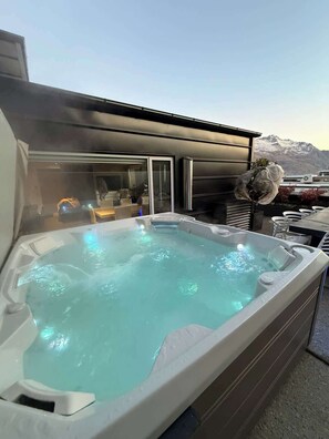 Un jacuzzi con vista a la montaña, un edificio moderno con amplios ventanales y zona de estar al aire libre.