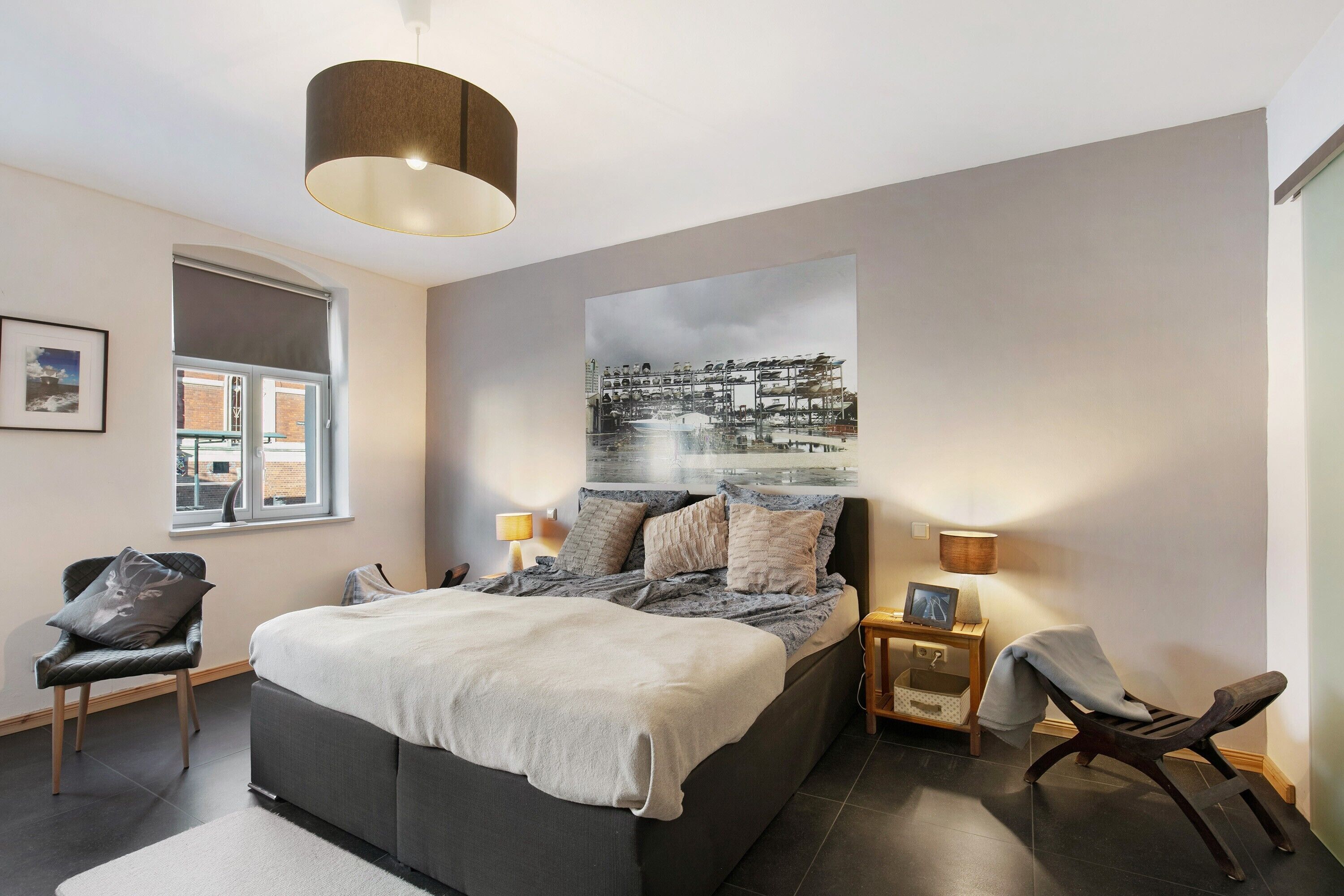 Une chambre à coucher comprenant un lit, deux tables de chevet, une chaise, une fenêtre et une lampe fixée au mur.