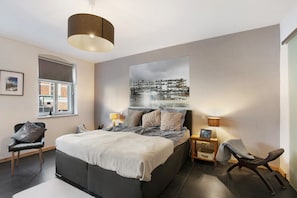 Een slaapkamer met een bed, twee nachtkastjes, een stoel, een raam en een wandlamp.