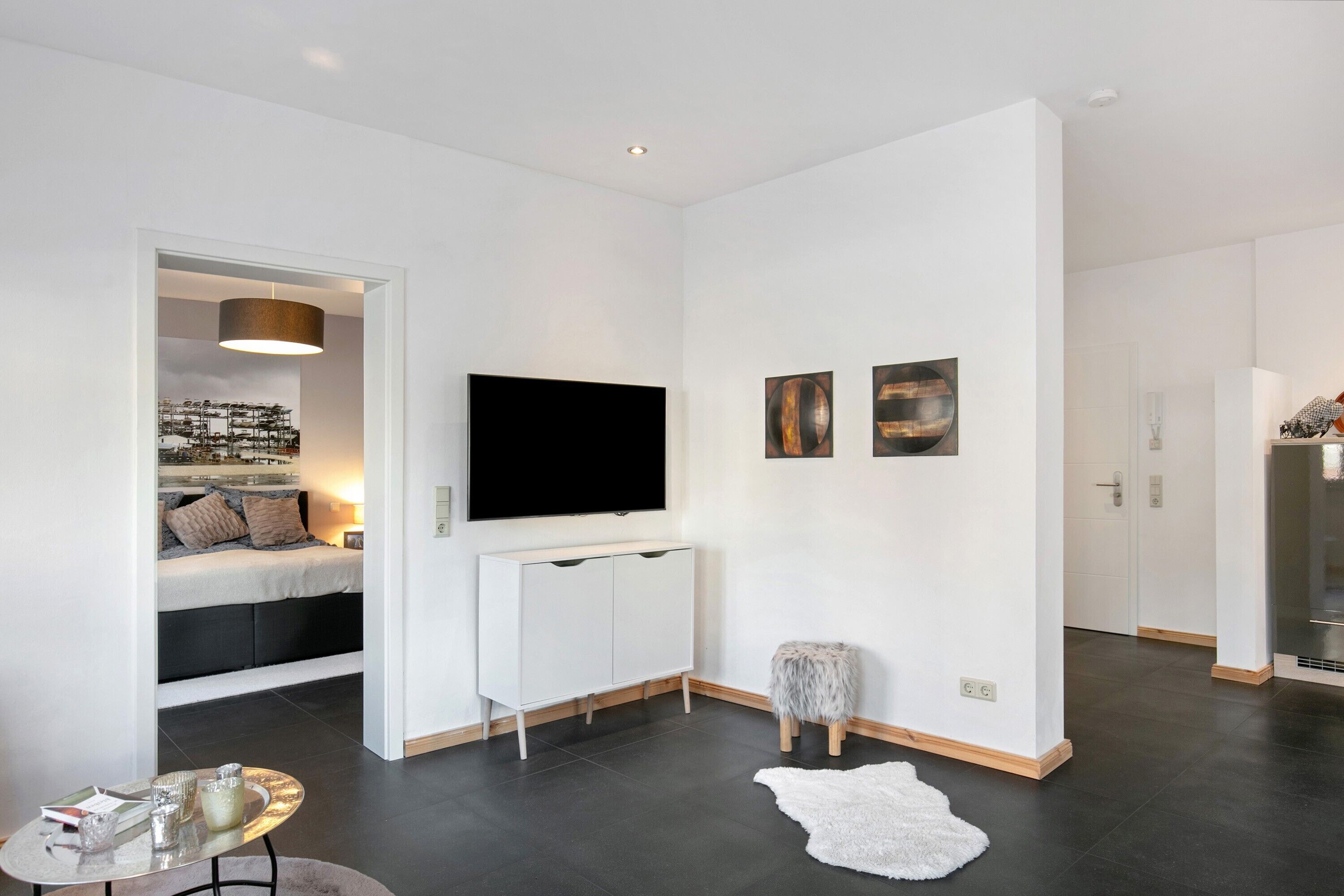 Ein modernes Wohnzimmer mit Flachbildfernseher, einer Couch, einem kleinen Tisch und einem weißen Teppich.
