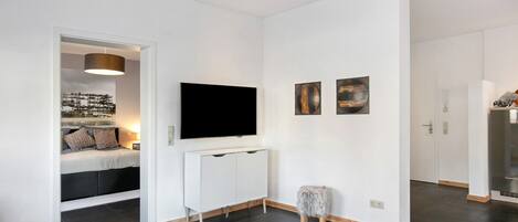 Ein modernes Wohnzimmer mit Flachbildfernseher, einer Couch, einem kleinen Tisch und einem weißen Teppich.