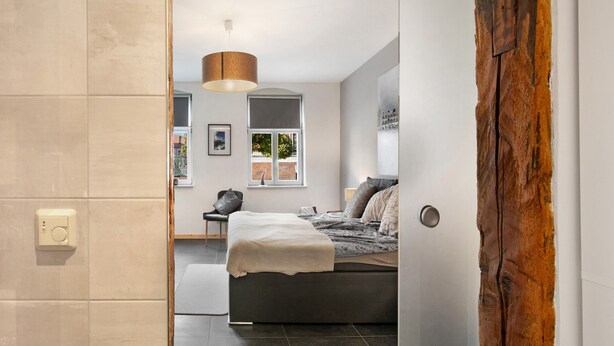 A bedroom with a bed, a hanging light fixture, a window, and a door.