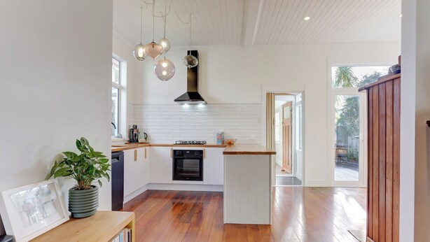 A modern kitchen with white cabinetry, a central island, a built-in oven, and pendant lighting. - The Blue House (Whanganui)