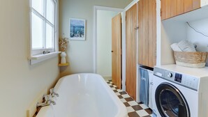 A modern bathroom with a bathtub, a washing machine, and wooden cabinets. - The Blue House (Whanganui)