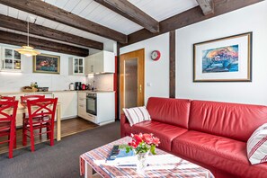 Een woonkamer met een rode leren bank, een eettafel met stoelen, een keukenhoek en een klok aan de muur.