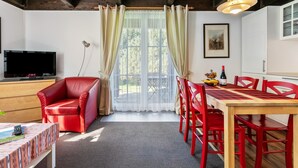A room with a television, a red chair, a dining table with red chairs, a window with curtains, and a painting on the wall. - Apartment 'Atlanta 201' with Private Terrace, Private Garden and Wi-Fi (Pellworm)