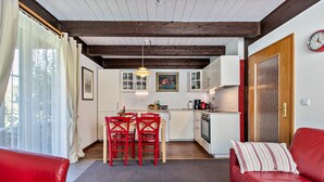 A cozy living room with a red sofa, a coffee table with flowers, and a kitchen in the background. - Apartment 'Atlanta 201' with Private Terrace, Private Garden and Wi-Fi (Pellworm)