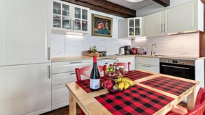 A kitchen with white cabinets, a wooden ceiling, a checkered tablecloth, a bottle of wine, and a fruit bowl. - Apartment 'Atlanta 201' with Private Terrace, Private Garden and Wi-Fi (Pellworm)