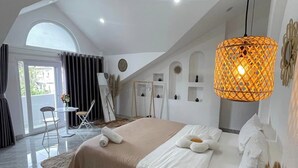 Un dormitorio moderno con una cama grande, una zona de estar con una mesa y sillas, una lámpara colgante y vistas a través de un amplio ventanal.