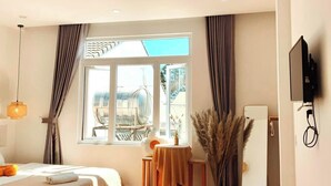 Una habitación de hotel moderna con suelo de madera, dos camas, un escritorio, una silla, un televisor y una ventana con cortinas.