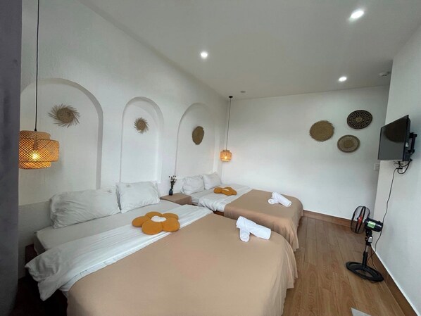 A hotel room with two beds, each with a beige bedspread and white pillows. There are decorative wall sconces and a flat-screen TV mounted on the wall.