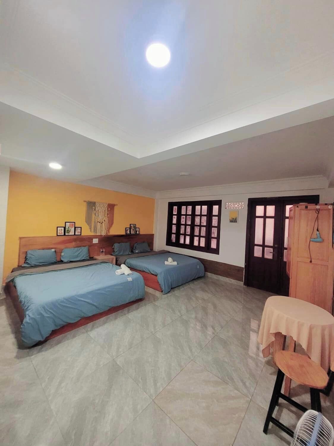 A room with three beds, a table with a chair, and a fan.