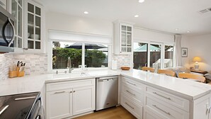 Een moderne keuken met witte kasten, een vaatwasser en een groot raam met uitzicht op de omgeving.