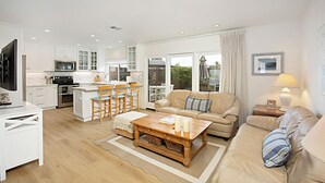 Een moderne keuken met witte kasten, een eethoek met houten stoelen, een beige bank en een salontafel.