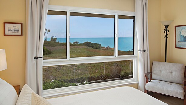 Een slaapkamer met een groot raam met uitzicht op zee en groen.