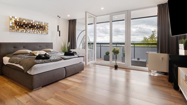 A modern bedroom with a large bed, a view to the outside, and a balcony with potted plants.