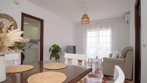Een moderne woonkamer met een eethoek, een bank, een televisie en een groot raam met gordijnen.