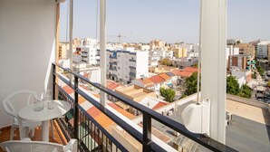Een balkon met een tafel en stoelen, met uitzicht op een stadsbeeld met verschillende gebouwen en een heldere lucht.