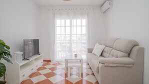 Een woonkamer met een beige bank, een televisie op een witte dressoir, een zwart-wit geruite vloer en een hanglamp.