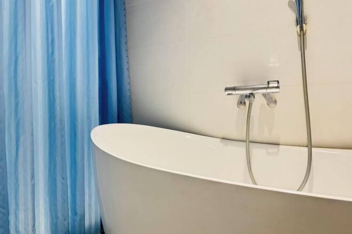 A bathtub with chrome fixtures and a shower head, a blue curtain, and a white tiled wall.