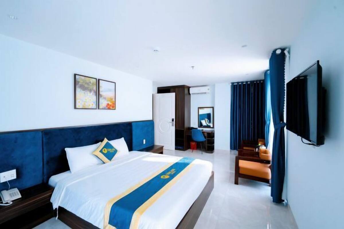A hotel room with a bed, a desk, a chair, a TV, and artwork on the wall.