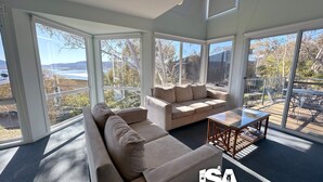 Ein geräumiger Wohnbereich mit einem beigefarbenen Sofa, einem Glastisch und großen Fenstern mit Blick ins Freie.