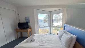 Ein Hotelzimmer mit Bett, Schreibtisch mit Fernseher und einem großen Fenster mit Blick auf das Meer.