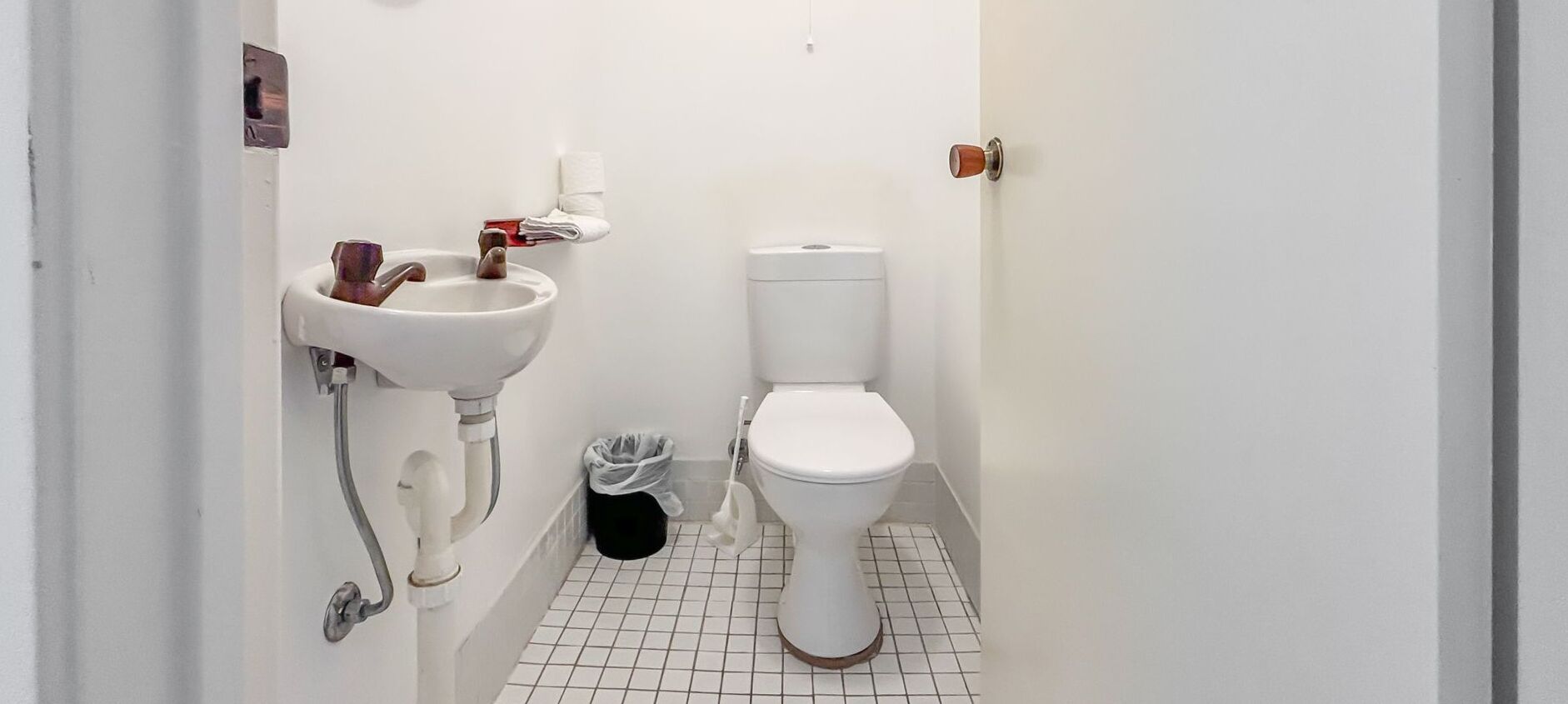 Een kleine, witte badkamer met een wastafel, toilet en een prullenbak.
