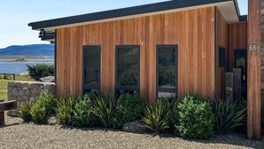 Edificio moderno con paneles de madera, amplias ventanas, una pared de piedra y vista a un lago.