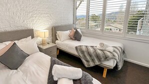 Une chambre avec deux lits, une table de chevet avec une lampe et une fenêtre avec des stores.