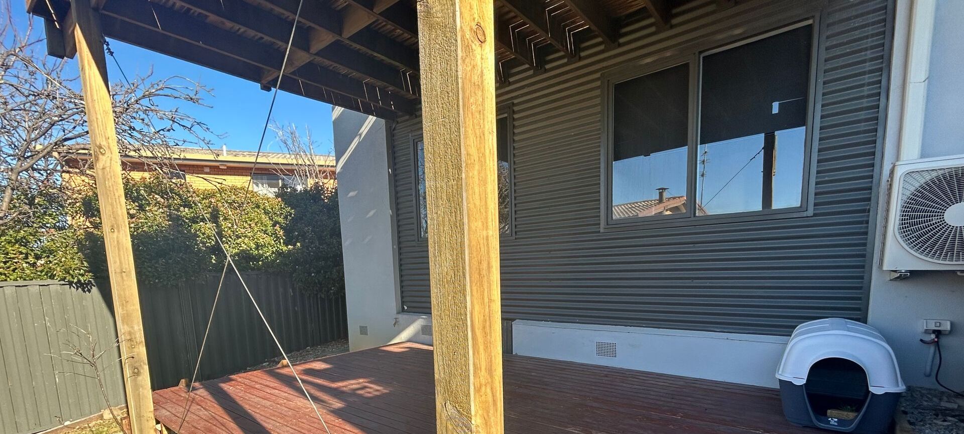 Un patio couvert avec une balançoire, une cour clôturée et une maison dont le garage est fermé et qui possède un bac à litière pour chat.