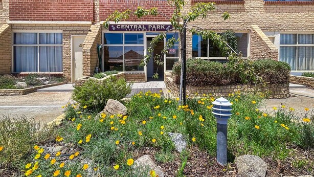 A building with a sign reading "Central Park Apartments" and a landscaped garden with yellow flowers.
