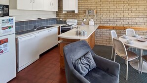 A compact kitchen with white cabinets, a built-in oven, and a dining area with white chairs and a table set for four.