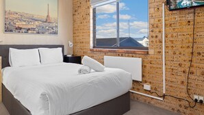 Habitación de hotel con cama, escritorio, ventana con vista a edificios y una pared de ladrillo.