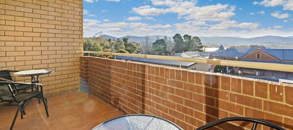 A balcony with a brick wall, a table, and two chairs. - Central Park 12 light two bedroom apartment (Jindabyne)