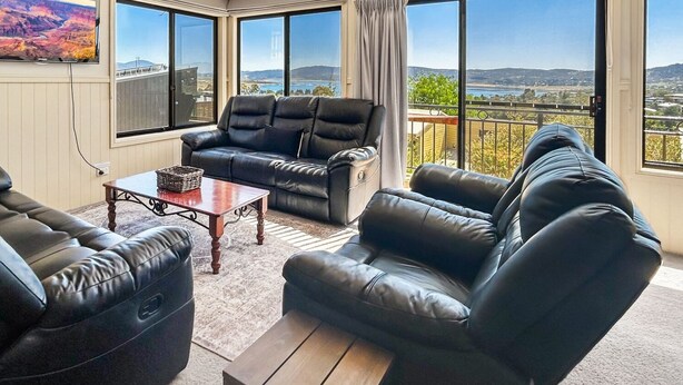 A living room with a black leather sofa set, a wooden coffee table, and a large window offering a scenic view.