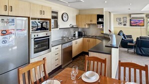 A modern kitchen with a dining area, a living room with a sofa, and a large window.