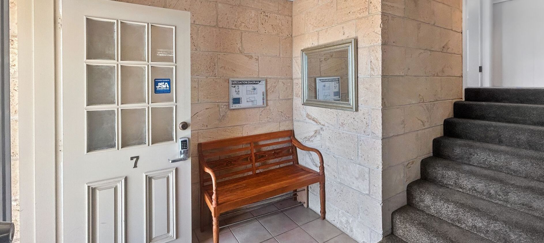 A door with a keypad lock, a bench, a stairway, and two evacuation diagrams on the wall.
