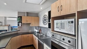A modern kitchen with wooden cabinets, a built-in oven, a microwave, and a stainless steel sink. - Dromaius 7 amazing lake and mountain views with double garage (Jindabyne)